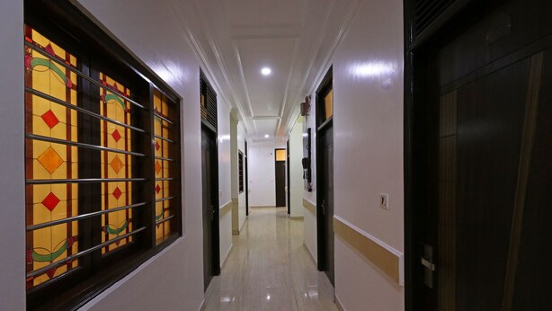 A hallway with a tiled floor, a door on the right, and a window with colorful patterns on the left. - OYO 10562 Paharganj (New Delhi)