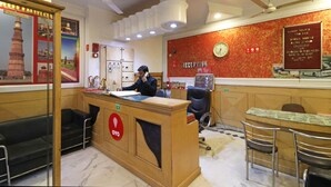 A reception area with a wooden desk, a clock, and a wall with a red patterned design. - OYO 10562 Paharganj (New Delhi)