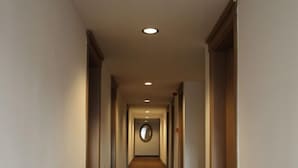 Un pasillo de hotel con alfombra estampada, puertas a ambos lados y un espejo redondo al fondo.