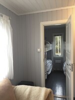 Una habitación con una cama litera, una ventana que da a árboles y una puerta que conduce a otra habitación.