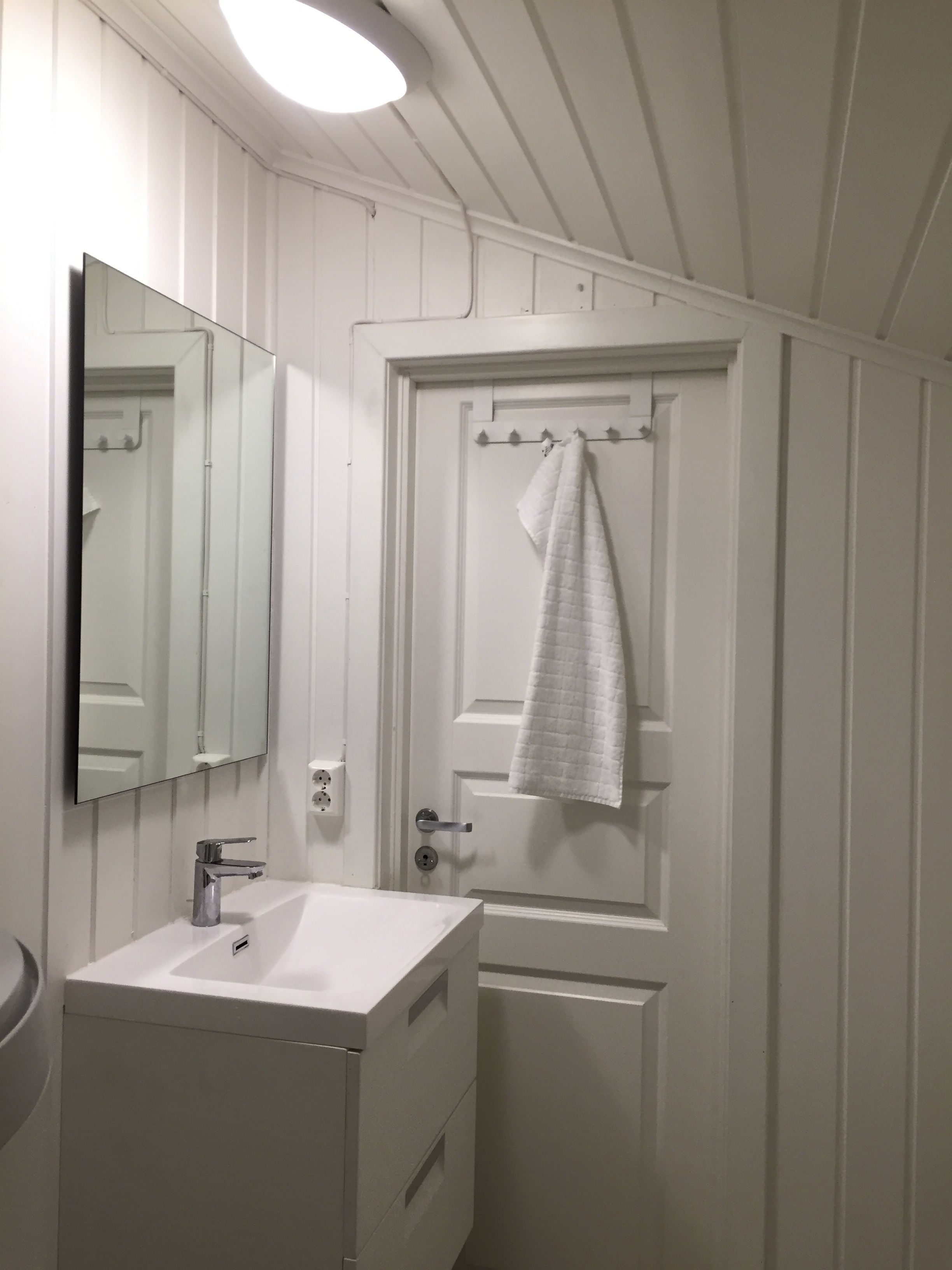 A bathroom with a white sink, a mirror, and a towel hanging on a door.