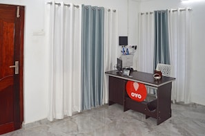 A room with a wooden door, a desk with a computer and a red circular sign, and curtains in white and blue.