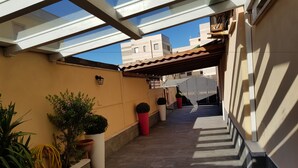 A covered outdoor corridor with potted plants, a tiled floor, and a view of buildings in the background. - La Lira (Fiumicino)