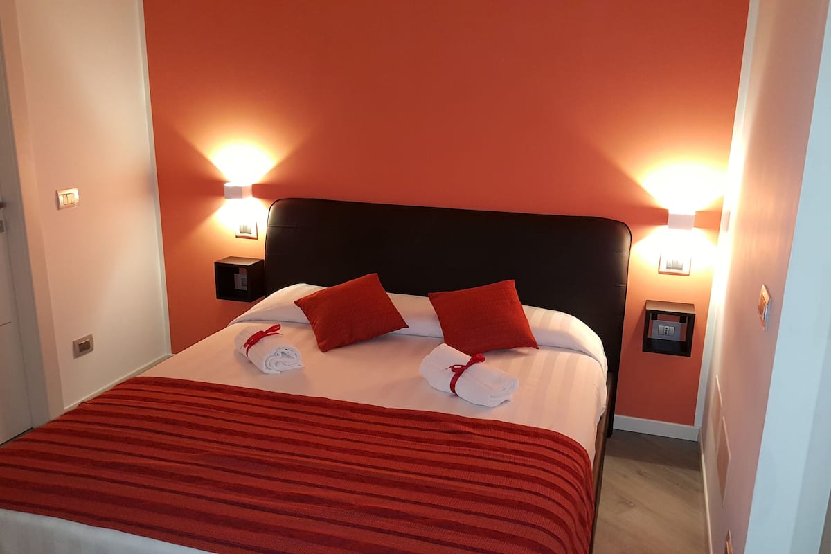 A hotel room with a bed, red pillows, and two wall-mounted lights.