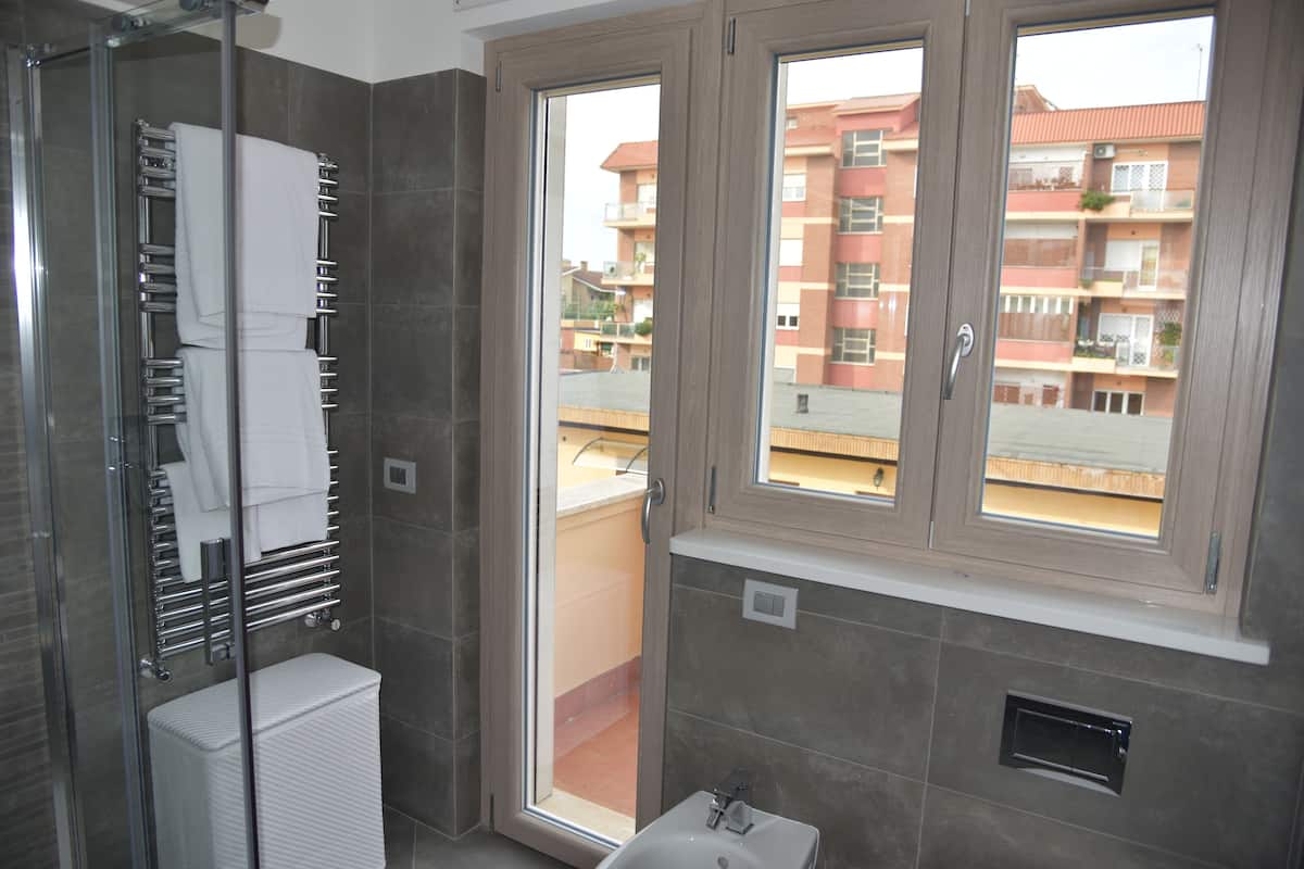 A bathroom with a glass shower enclosure, a white sink, and a window with a view of a residential building.