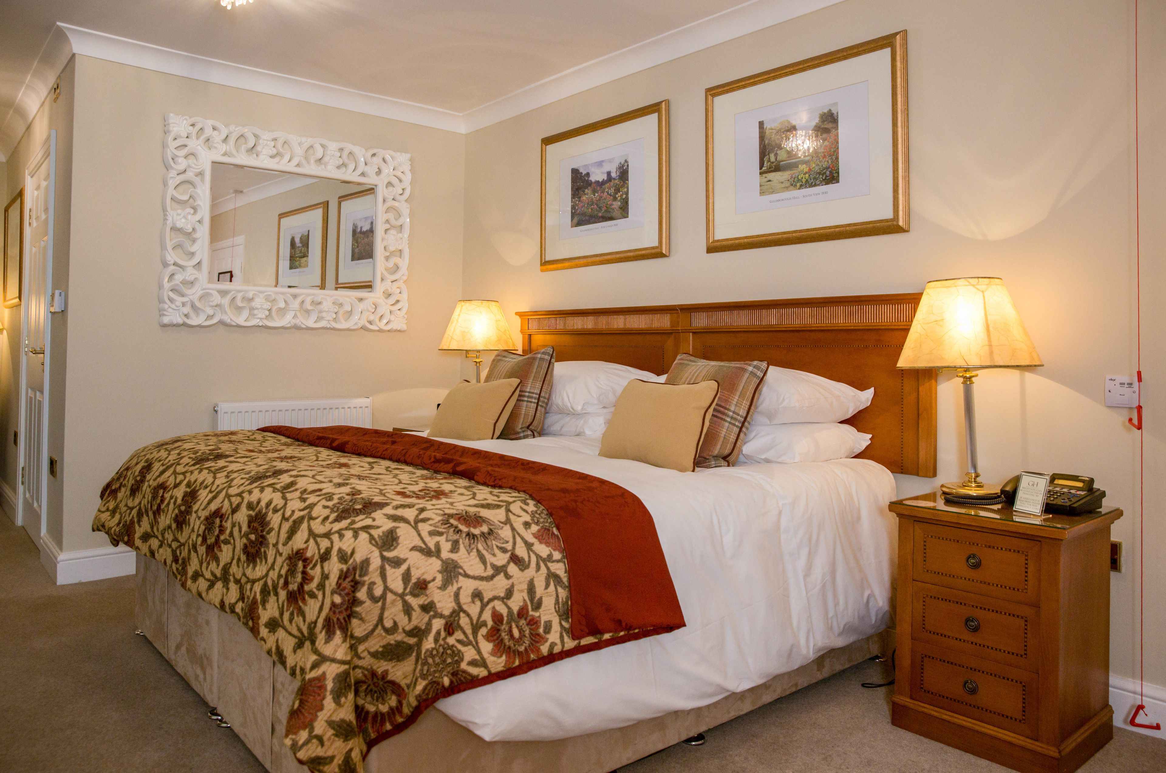 A neatly made bed with a floral bedspread, two bedside lamps, a nightstand with a phone, and framed pictures on the wall.