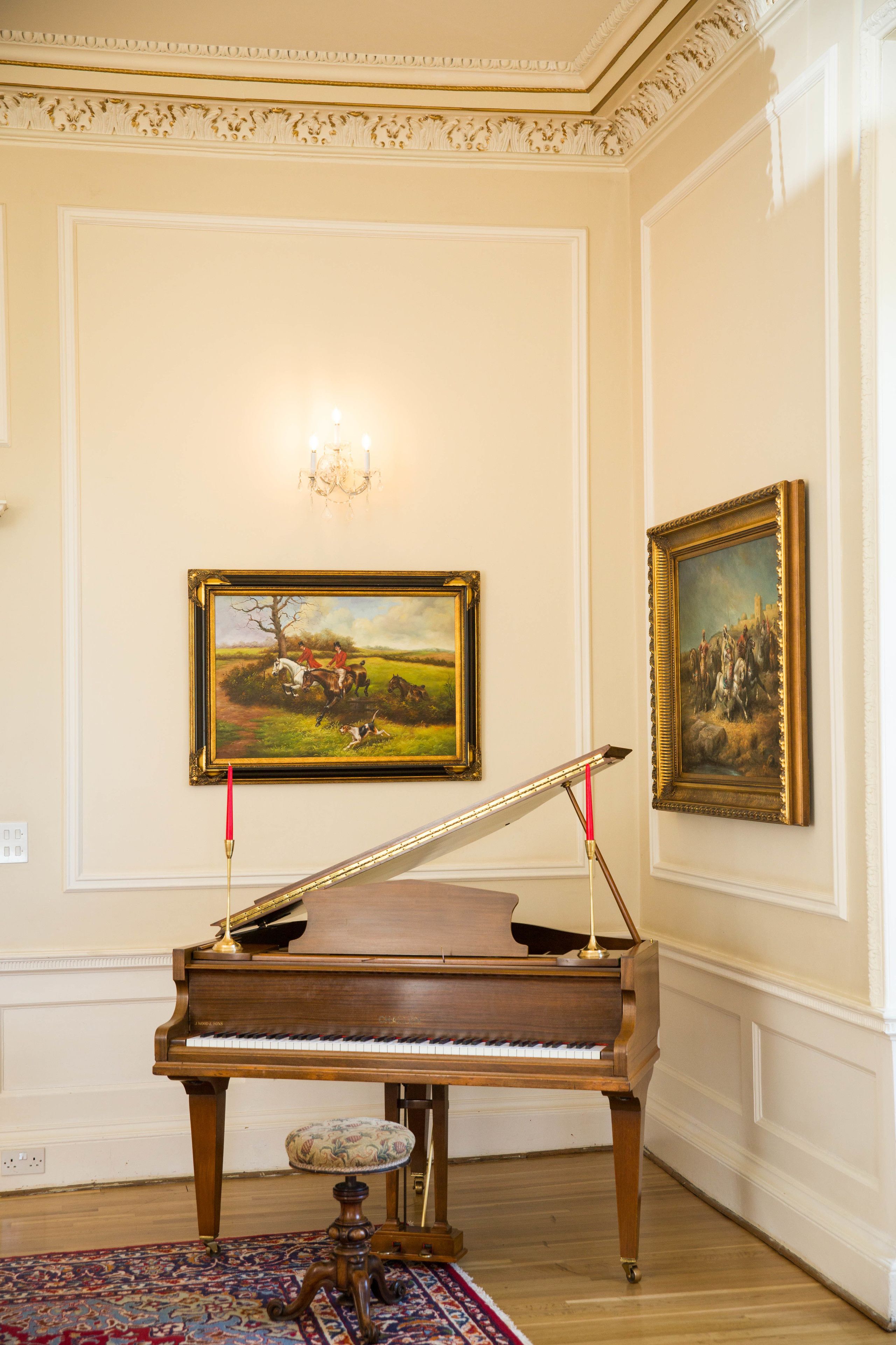 A grand piano in a room with ornate wall moldings and two framed paintings.