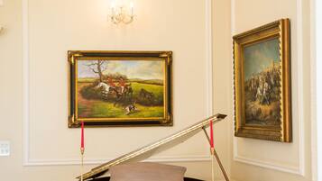 A grand piano in a room with ornate wall moldings and two framed paintings.