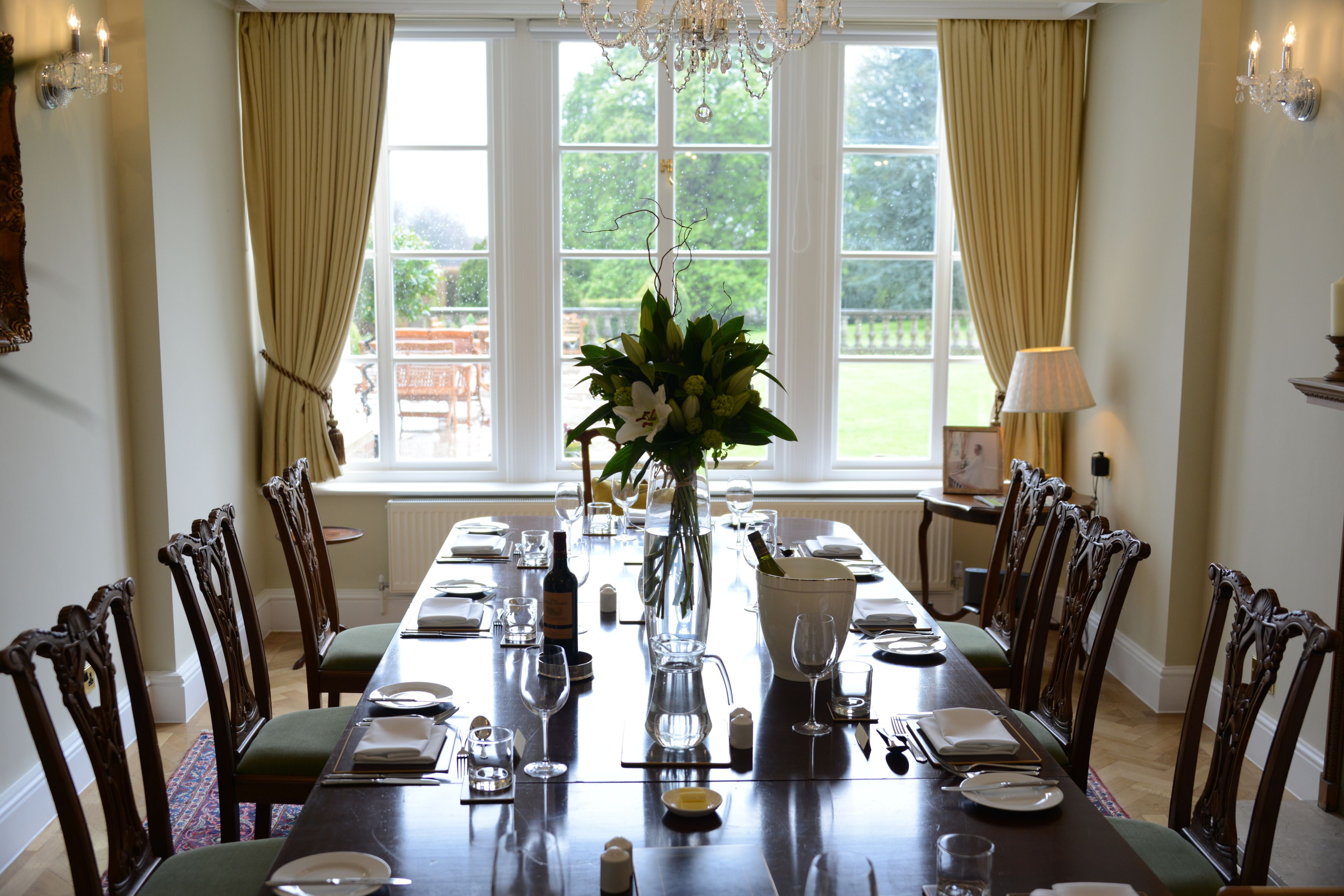 A dining room with a long table set for a meal, surrounded by chairs, a vase with flowers, and a chandelier.