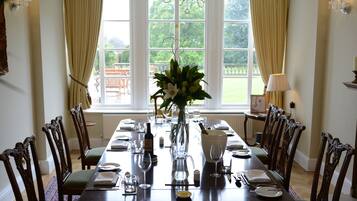 A dining room with a long table set for a meal, surrounded by chairs, a vase with flowers, and a chandelier.