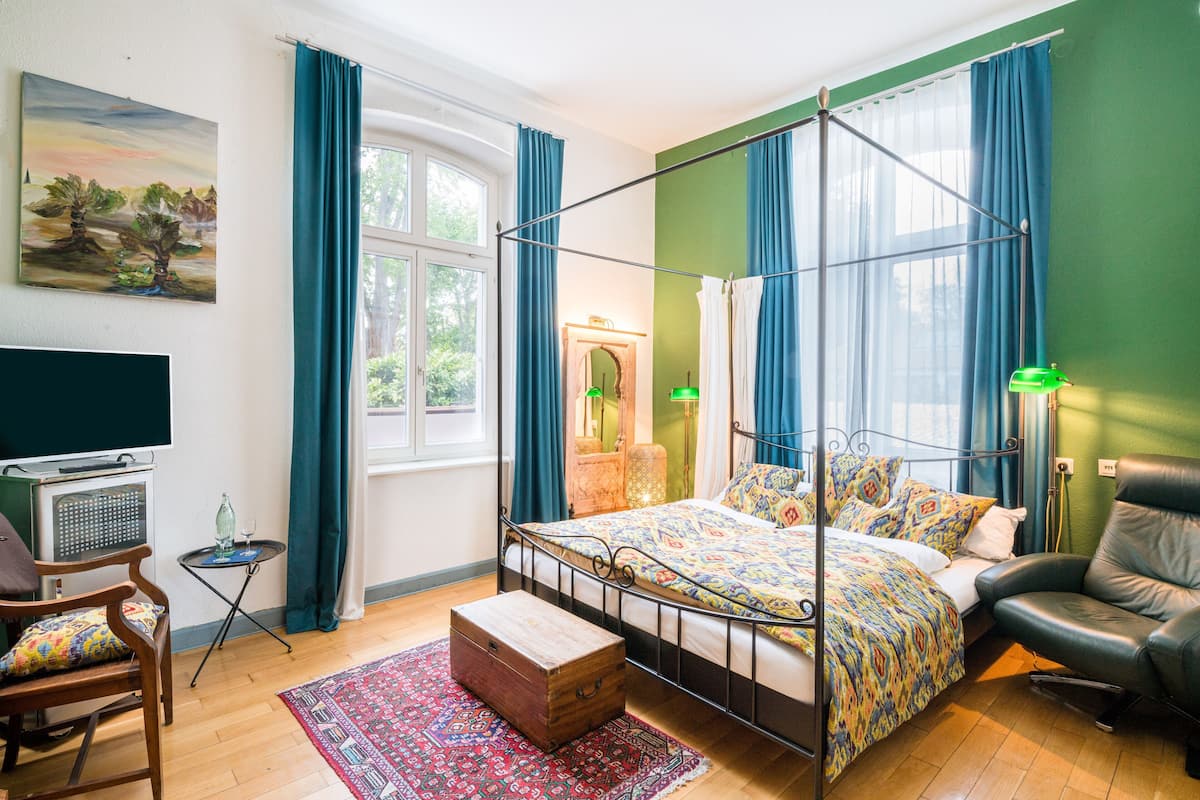 Een hemelbed met een bedsprei met patroon, een houten dressoir, een televisie op een standaard en een groene wand.