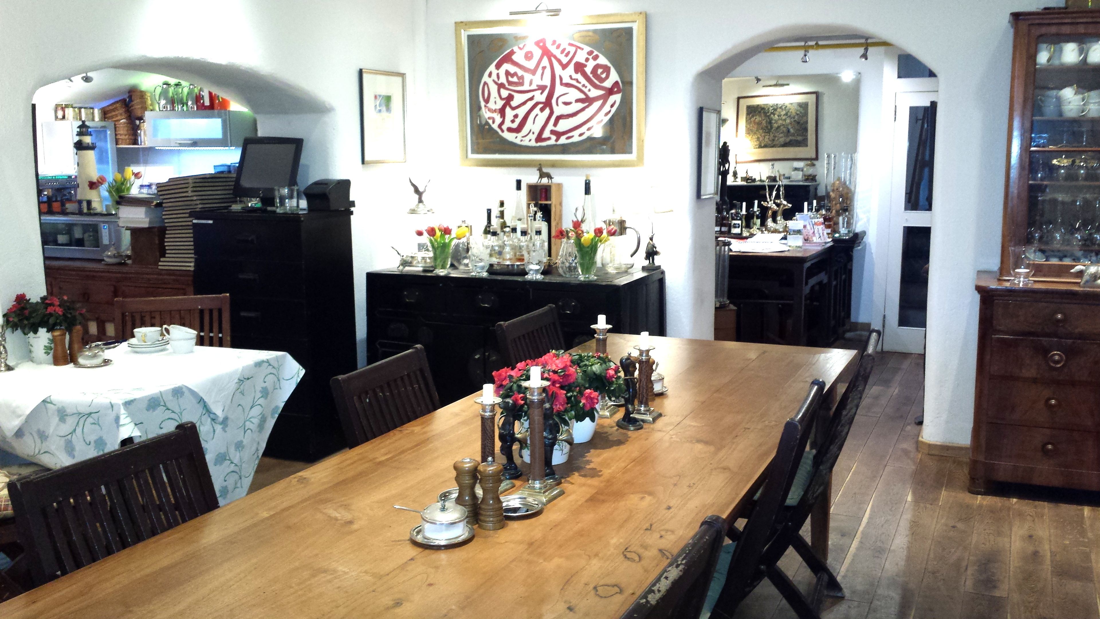 A dining area with a wooden table set for four, surrounded by chairs. A large decorative piece hangs above the table, and various items are displayed on the walls and shelves.