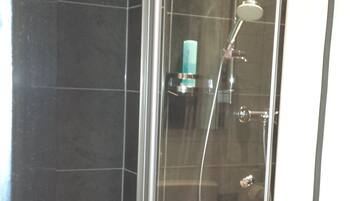 A glass-enclosed shower stall with a handheld showerhead and a wall-mounted faucet.
