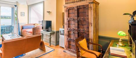 Una habitación con un armario de madera, un sofá, una silla, un escritorio con una lámpara y vistas a un balcón.