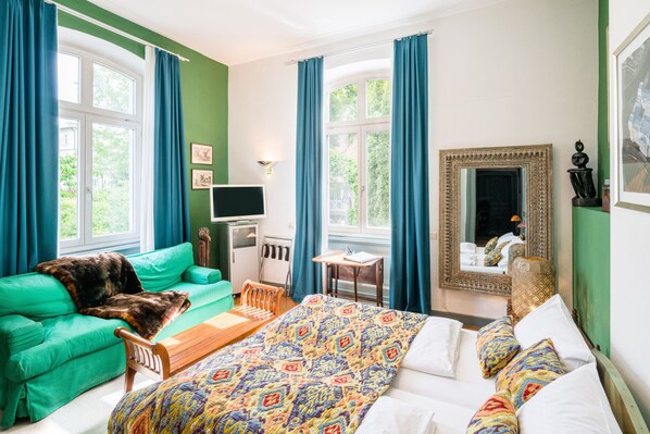 Une pièce comprenant un lit, un canapé vert, un banc en bois, une petite table et un miroir.