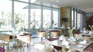 Un restaurante moderno con ventanas amplias, mesas redondas y sillas acolchadas.