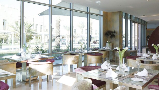Un restaurant moderne doté de grandes fenêtres, de tables rondes et de chaises rembourrées.