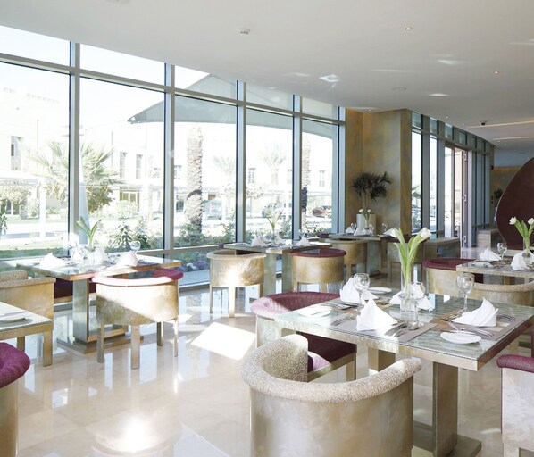 Un restaurant moderne doté de grandes fenêtres, de tables rondes et de chaises rembourrées.