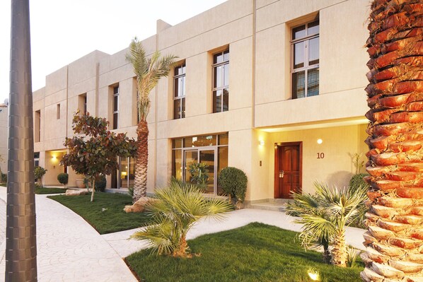 A modern building with a flat facade, multiple windows, and a well-maintained lawn with palm trees. - Vivienda Hotel Villas Granada (Riyadh)