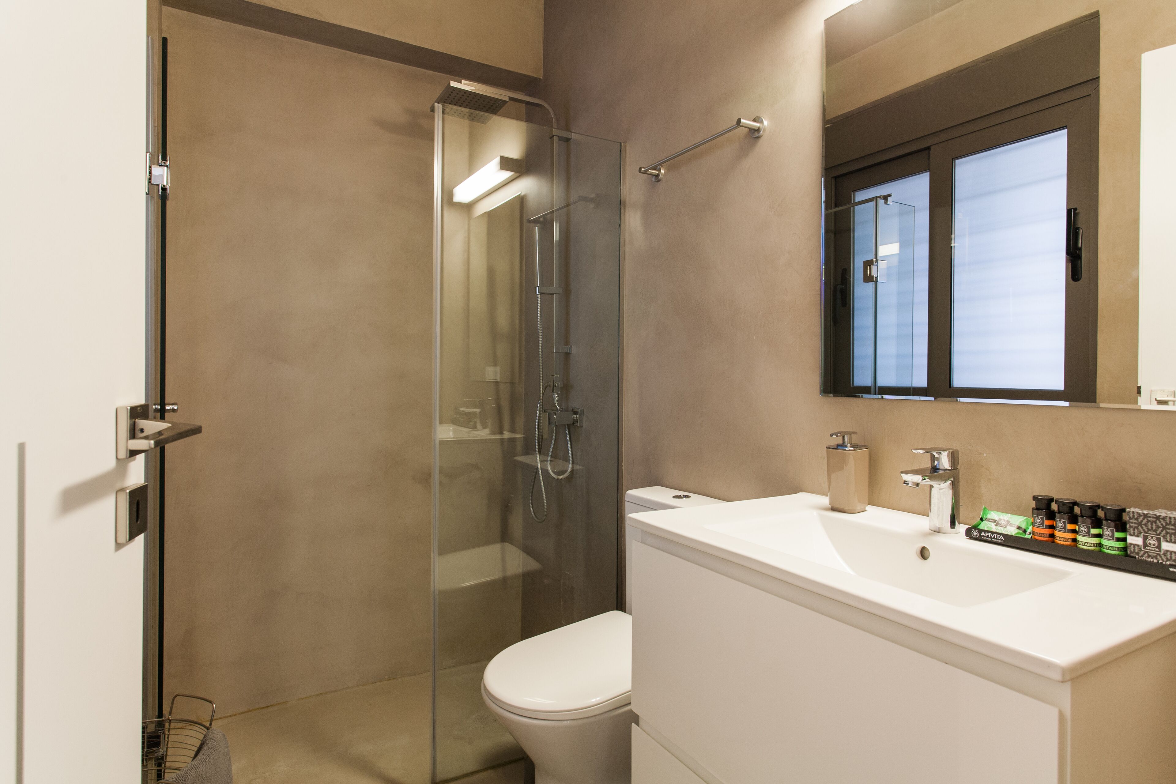 A modern bathroom with a glass-enclosed shower, a white toilet, and a sink with toiletries.