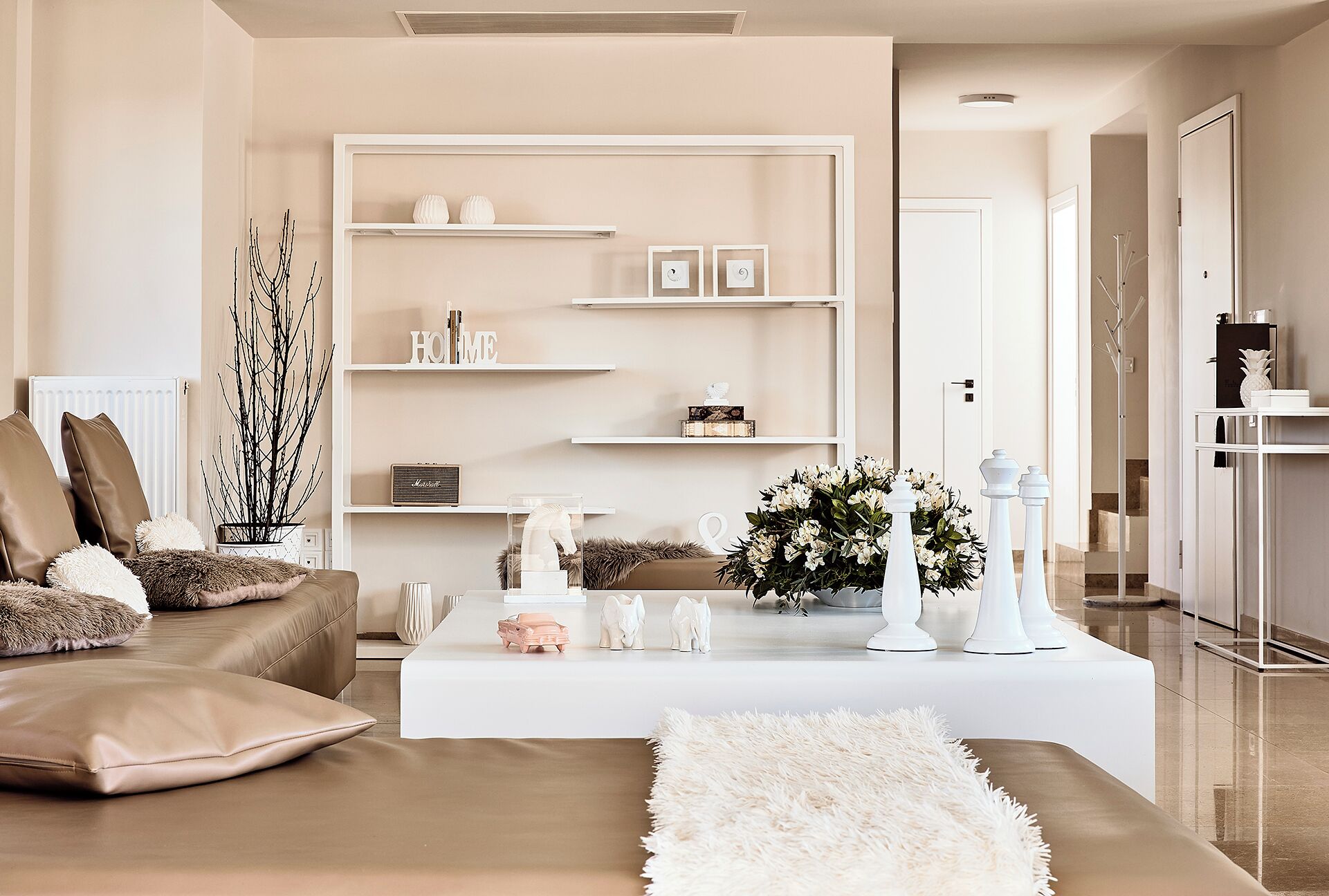 Una sala de estar moderna con un sofá color beige, una mesa de centro blanca y una estantería.