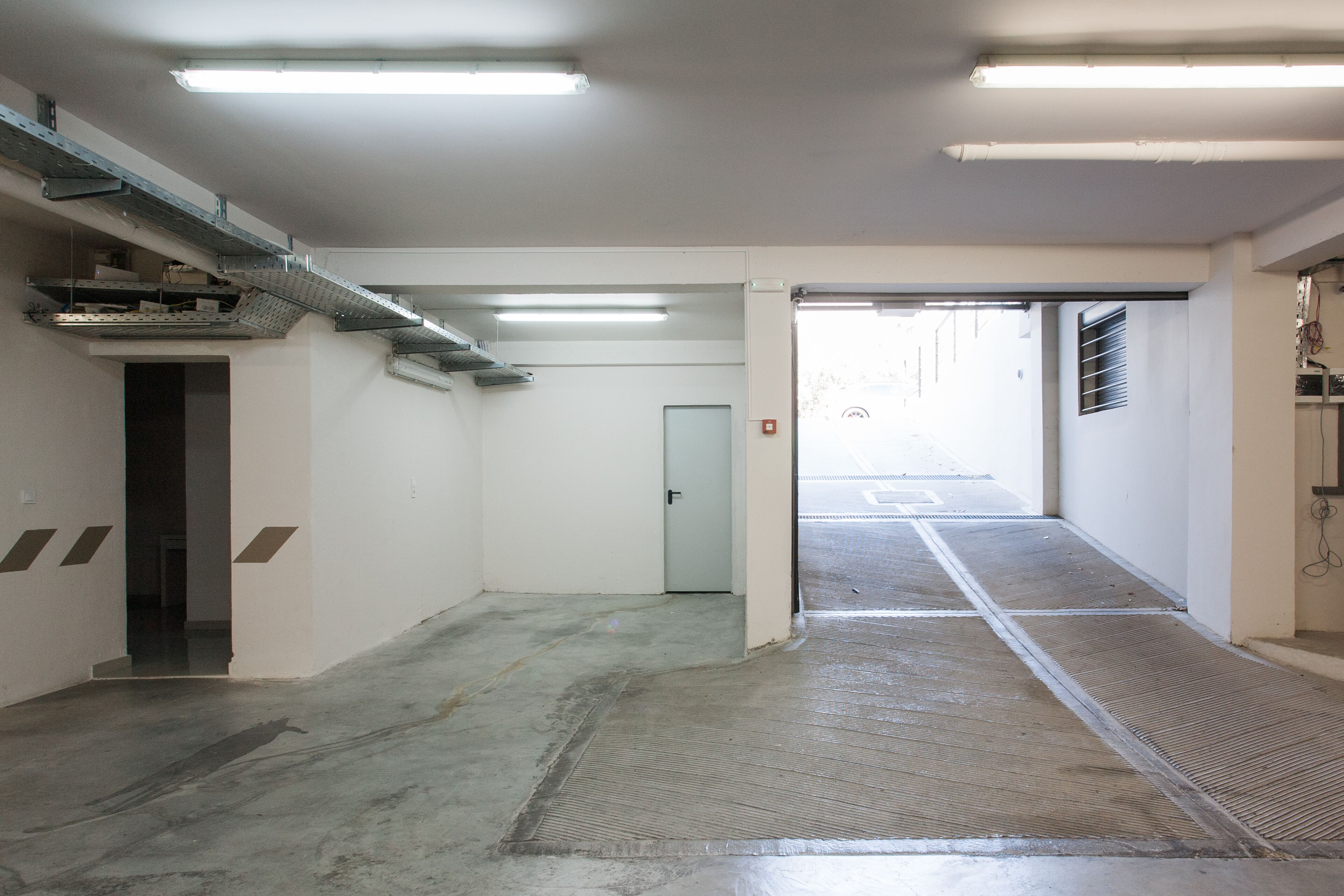 A hallway with a door, a ramp, and a ceiling with fluorescent lights.