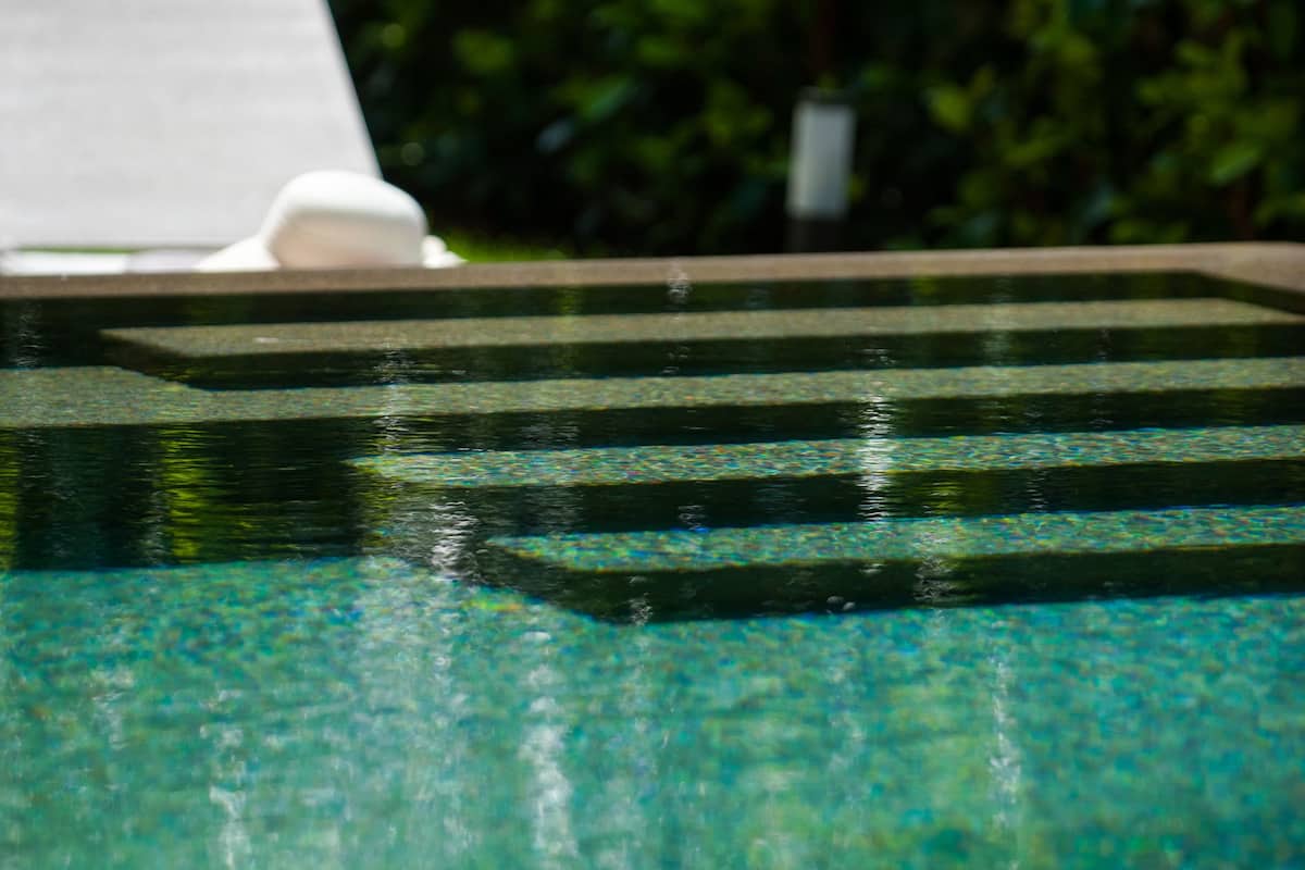 Una piscina con escalones de acceso, rodeada de vegetación.