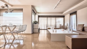 A modern living room with a dining area, a sofa, and a coffee table. - Crystal Green Signature Apartments Glyfada (Glyfada)