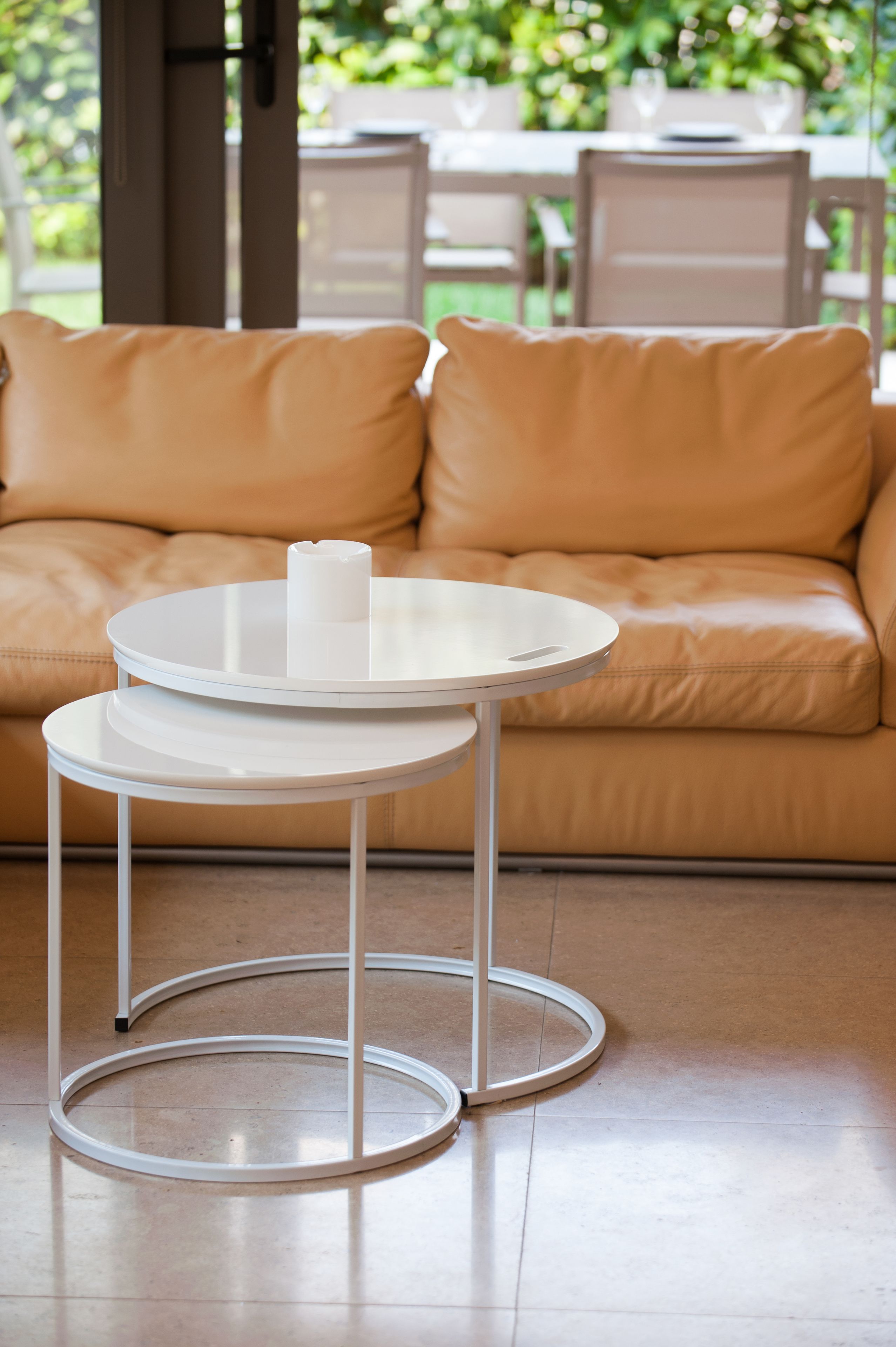 A round white table with a candle on it, placed in front of a tan leather sofa.