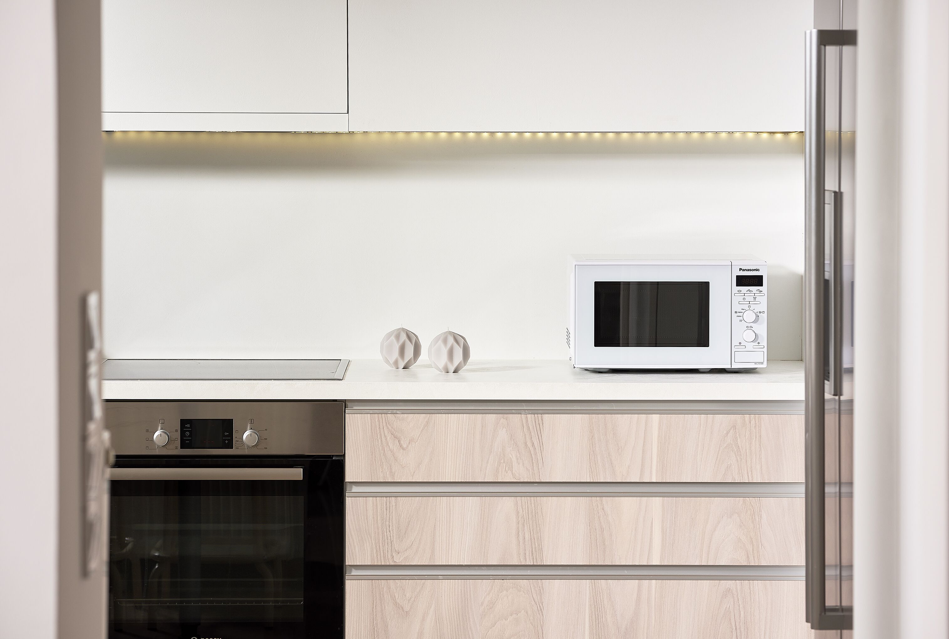 Een moderne keuken met een ingebouwde magnetron, oven en houten kastjes.