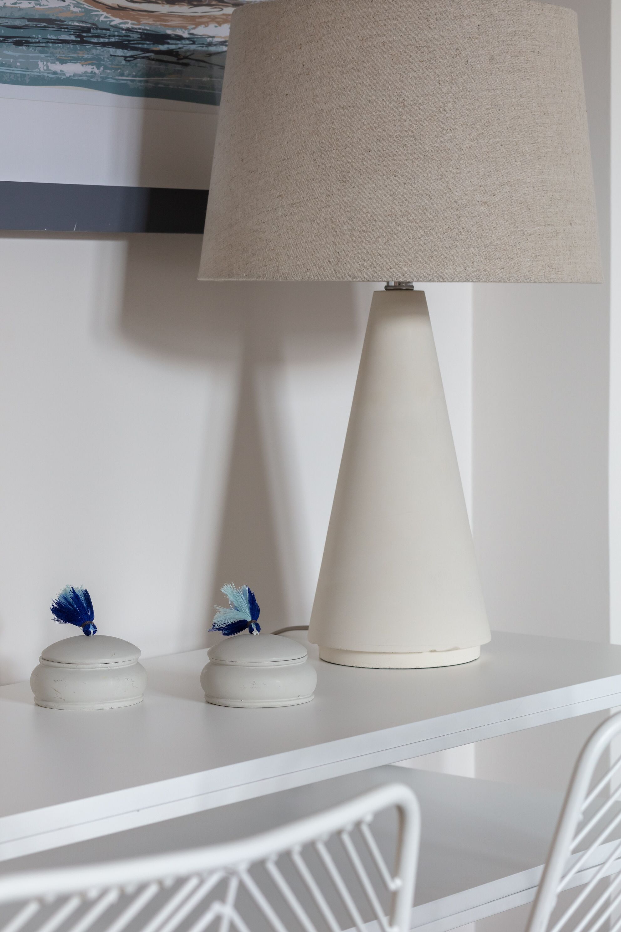 Een wit bureau met een lamp, twee kleine bakjes en een stoel.