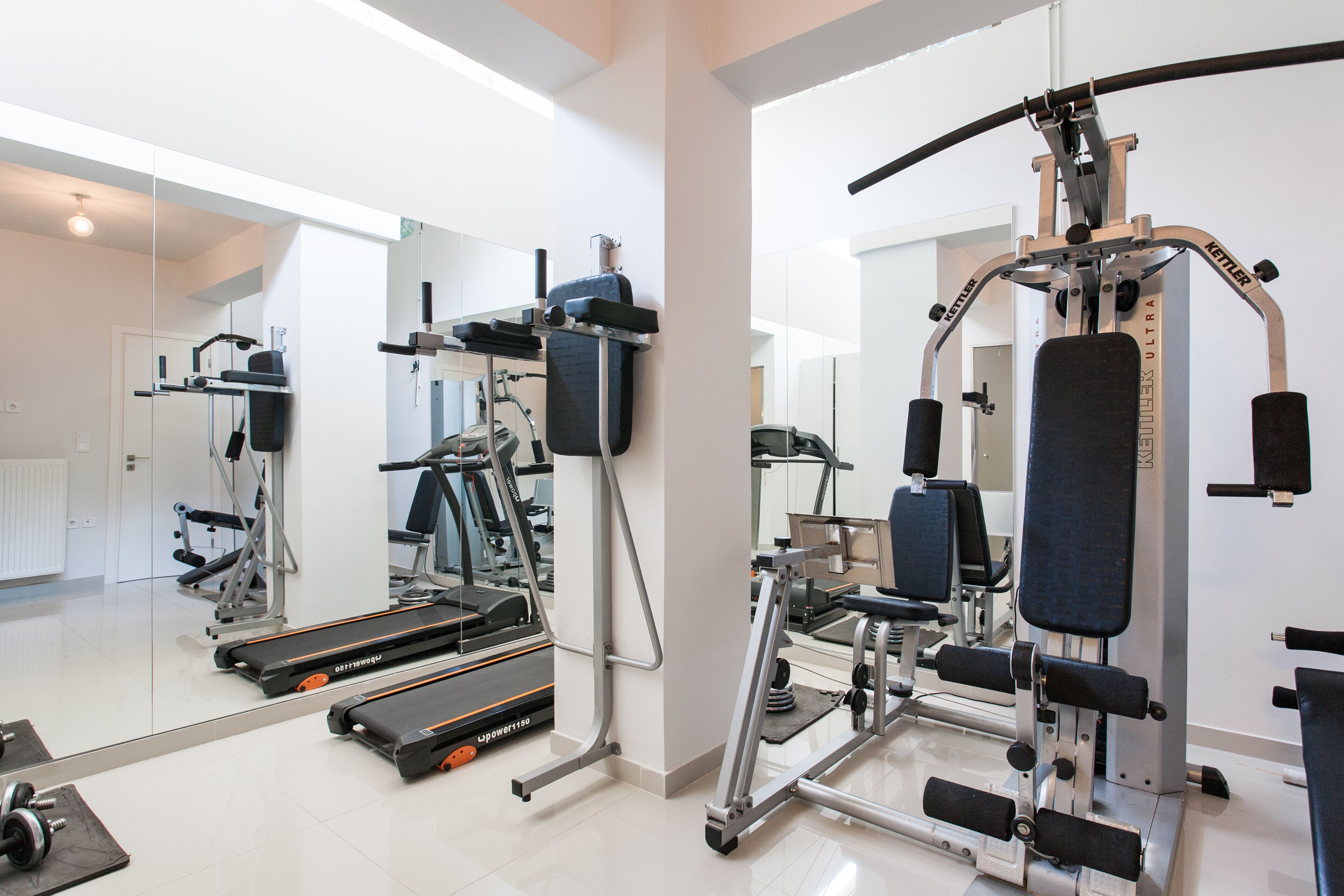 Une salle de sport équipée de matériel d’exercice, d’un tapis de course et d’un miroir qui reflète l’espace.
