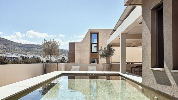 A modern building with a pool, outdoor seating, and a view of the surrounding landscape. - Crystal Green Signature Apartments Glyfada (Glyfada)