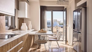 A modern kitchen with a dining area, large windows, and a view of the city. - Crystal Green Signature Apartments Glyfada (Glyfada)