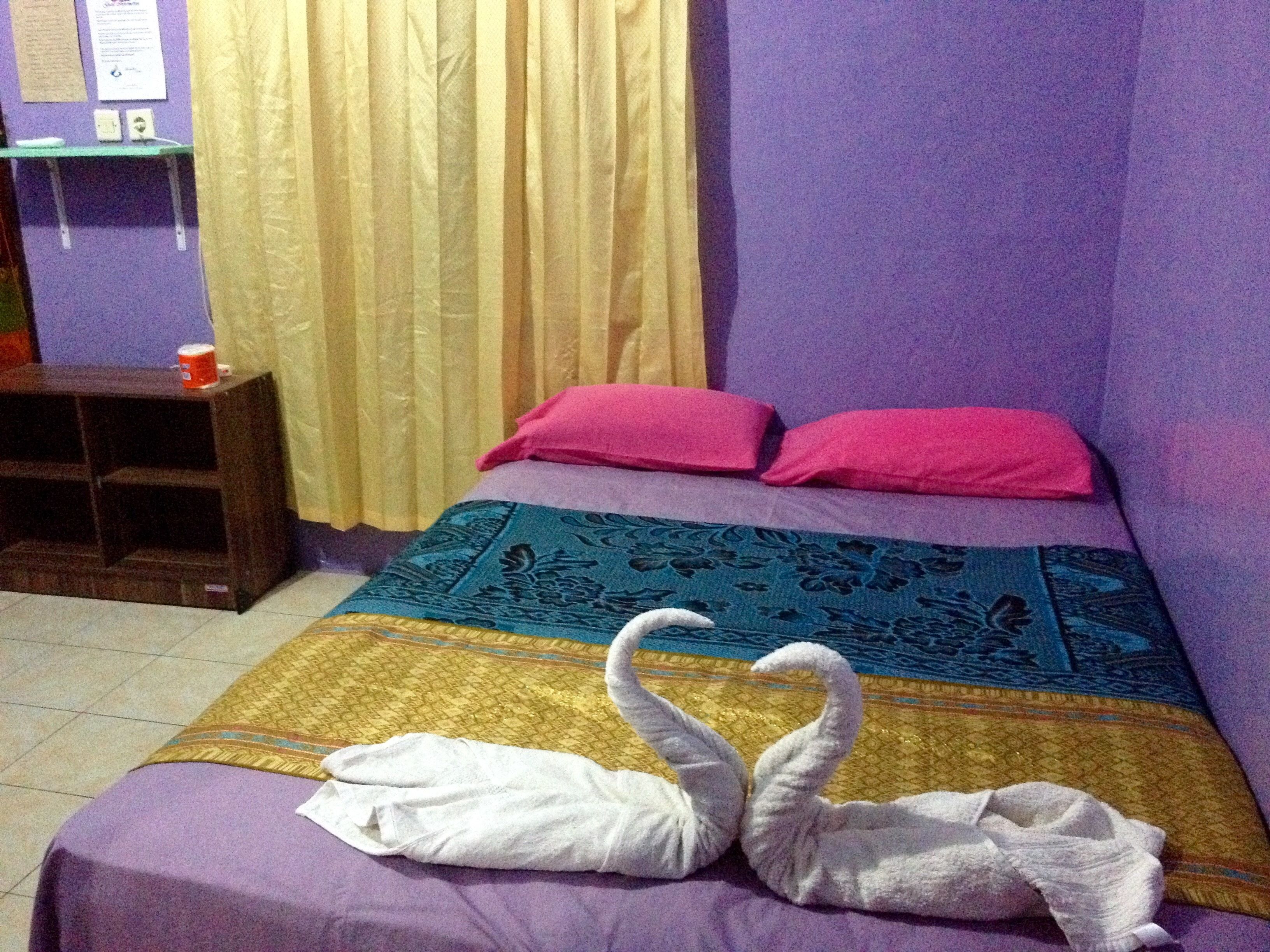 A room with a bed, a purple wall, a curtain, and a small table with a cup.