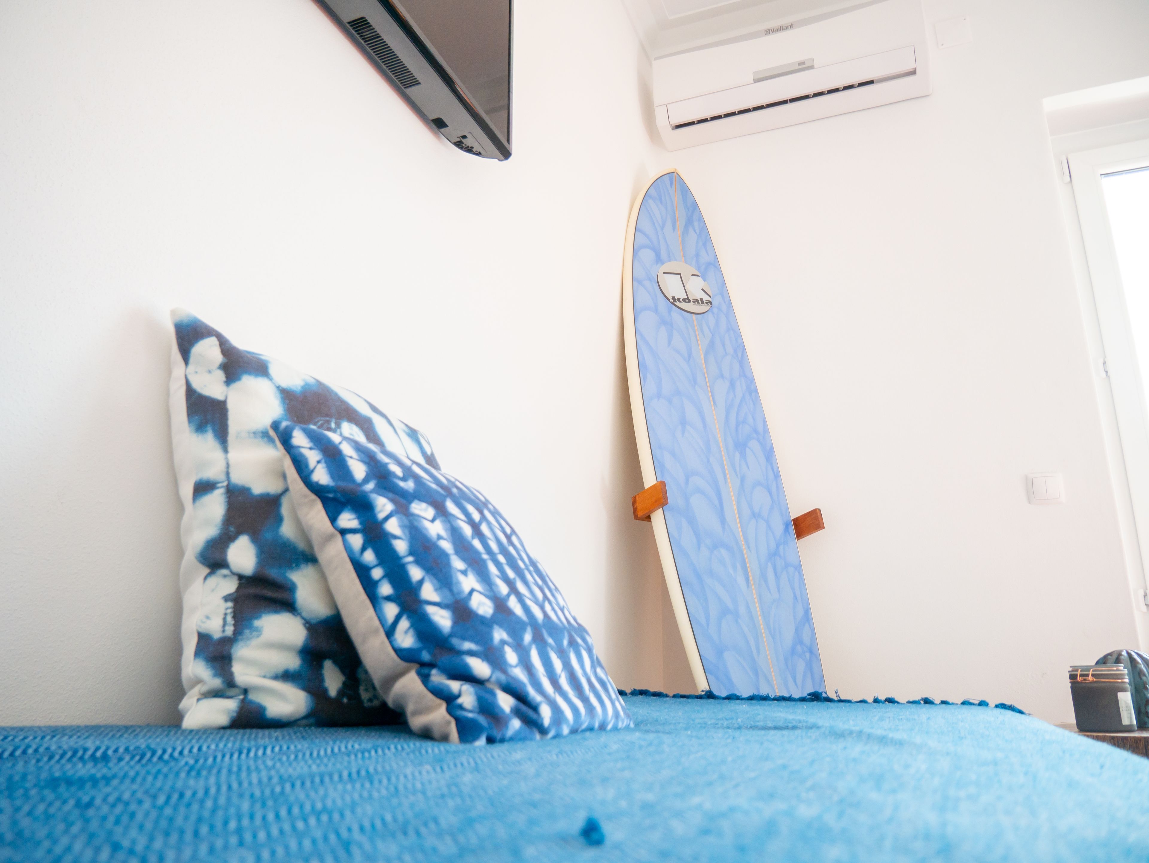 Ein Schlafzimmer mit einem Bett, einem blau-weißen Kissen und einem blauen Surfbrett, das an der Wand lehnt.