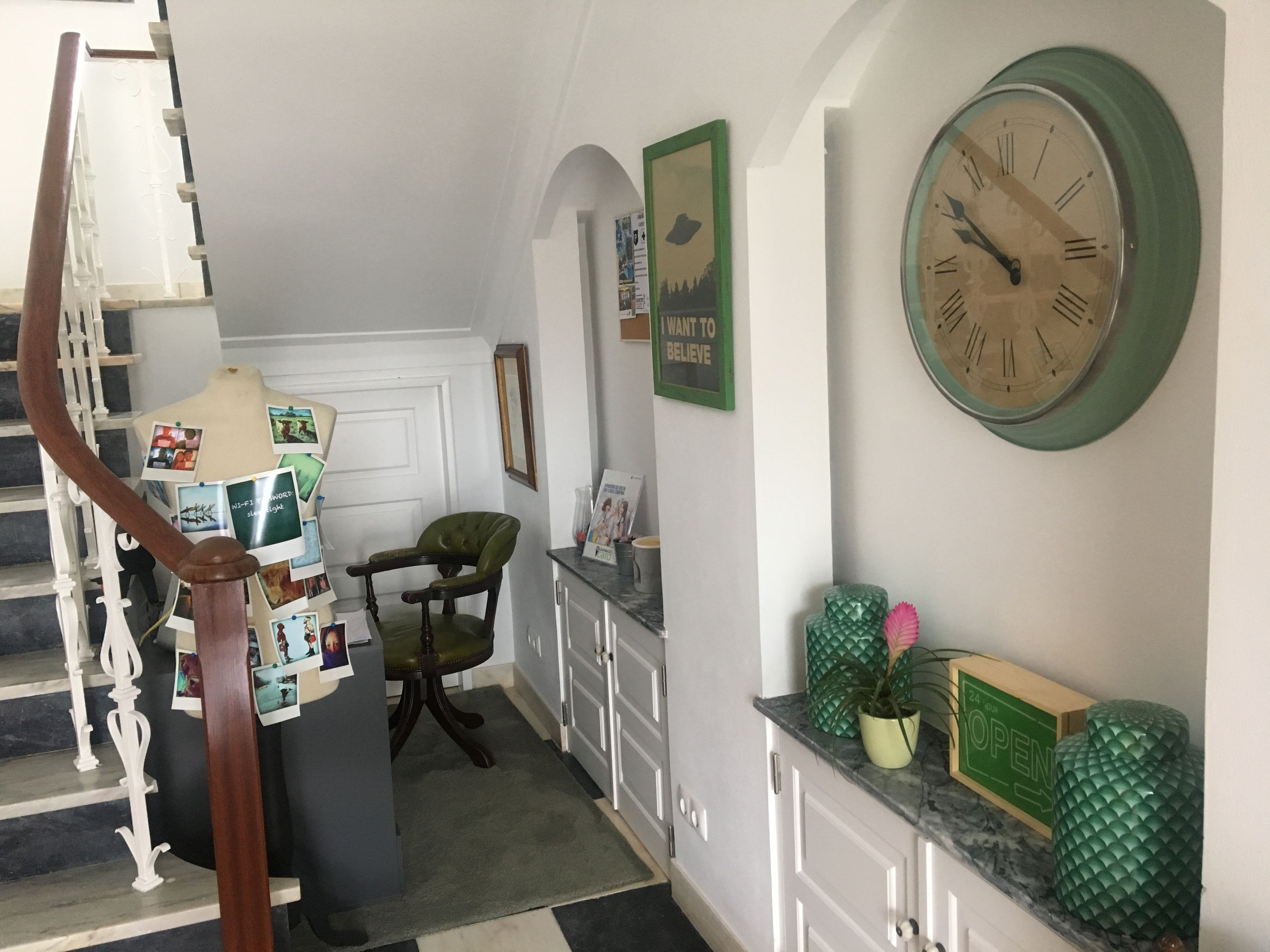 A staircase with a wooden handrail, a green upholstered chair, a wall clock, and a small potted plant.