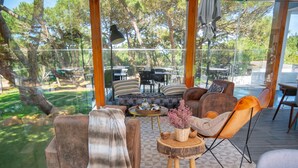 Uma área de estar moderna ao ar livre, com sofás de couro e uma mesa de centro de madeira, com vista para uma piscina e vegetação exuberante.