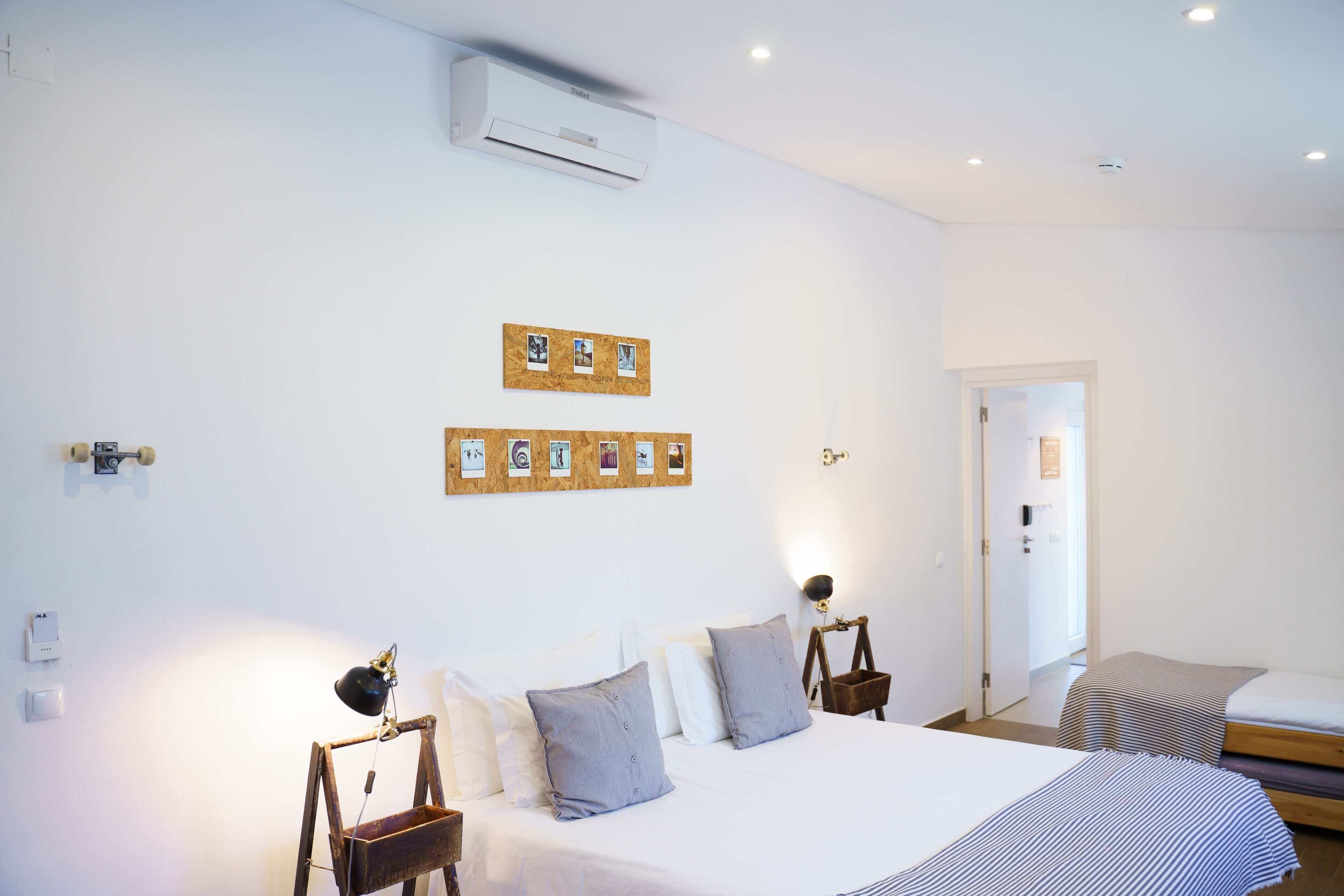 Un dormitorio con una cama grande, mesitas de noche, aire acondicionado instalado en la pared y una puerta que da a otra habitación.