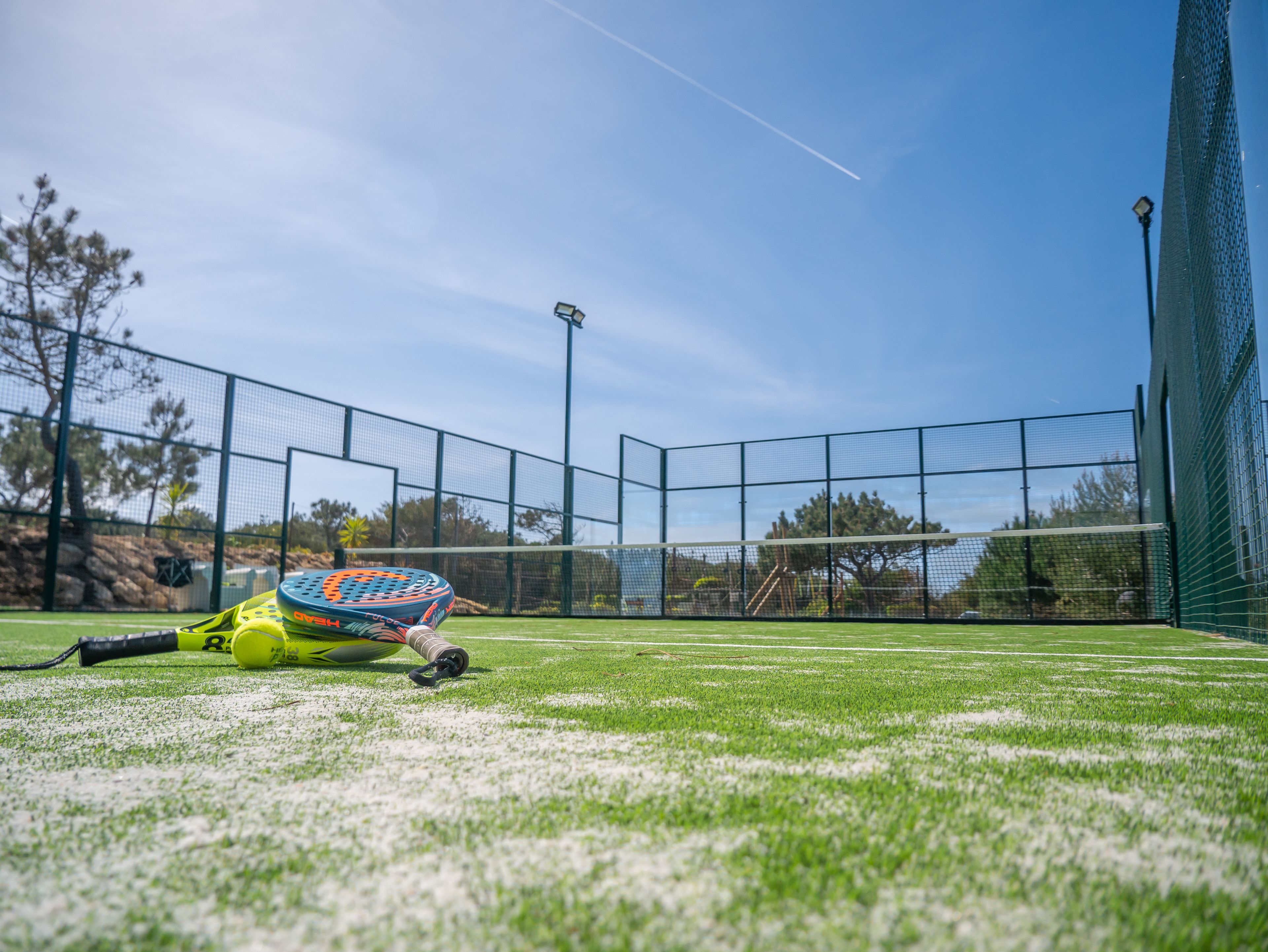 A tennis court with a net, a tennis ball, and a racket on the ground.