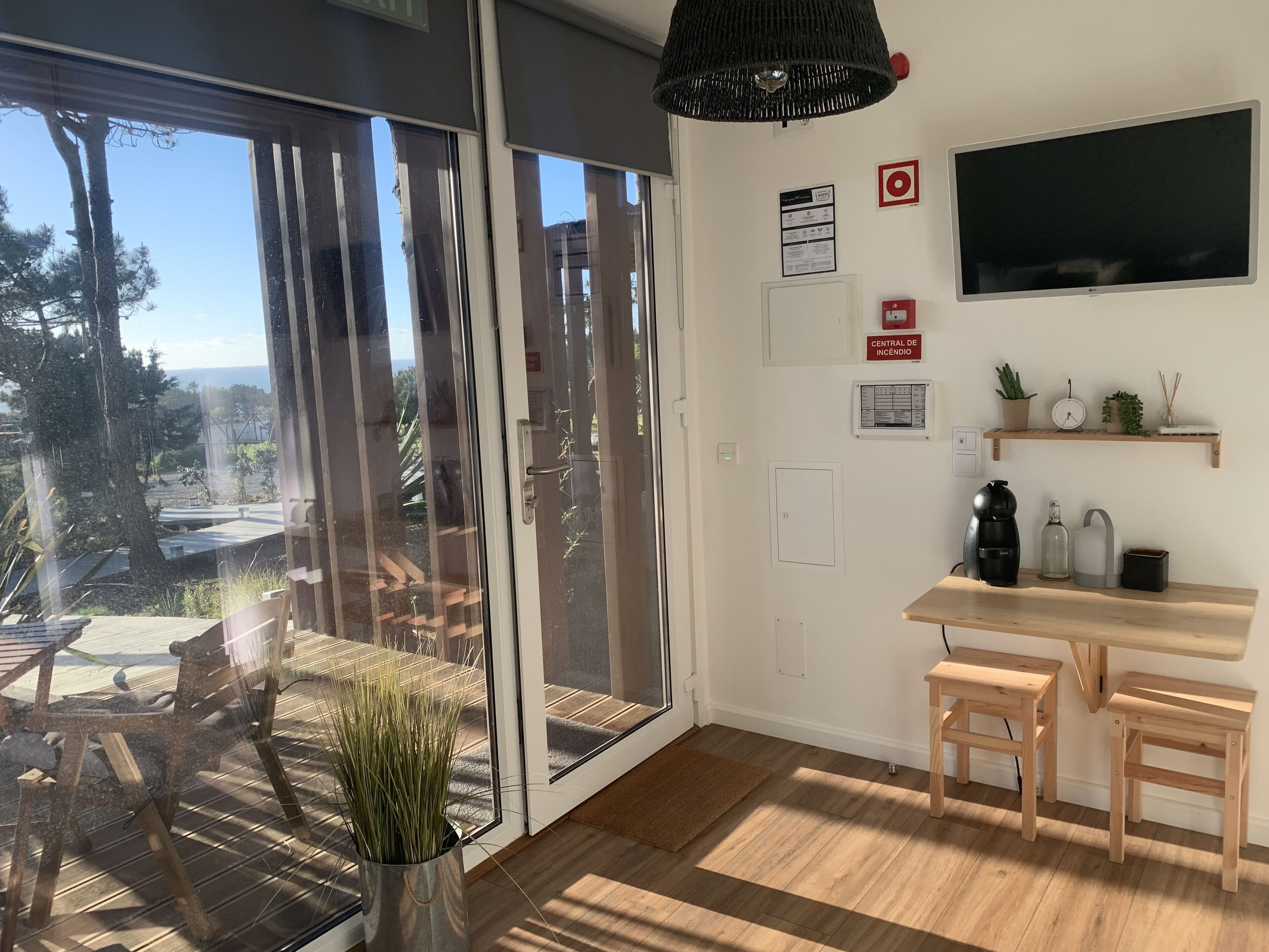 A modern interior with a sliding glass door leading to an outdoor area, a wooden floor, a small wooden table, and a shelf with decorative items.