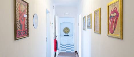 A hallway with framed posters, a chandelier, and a checkered floor leading to a room.