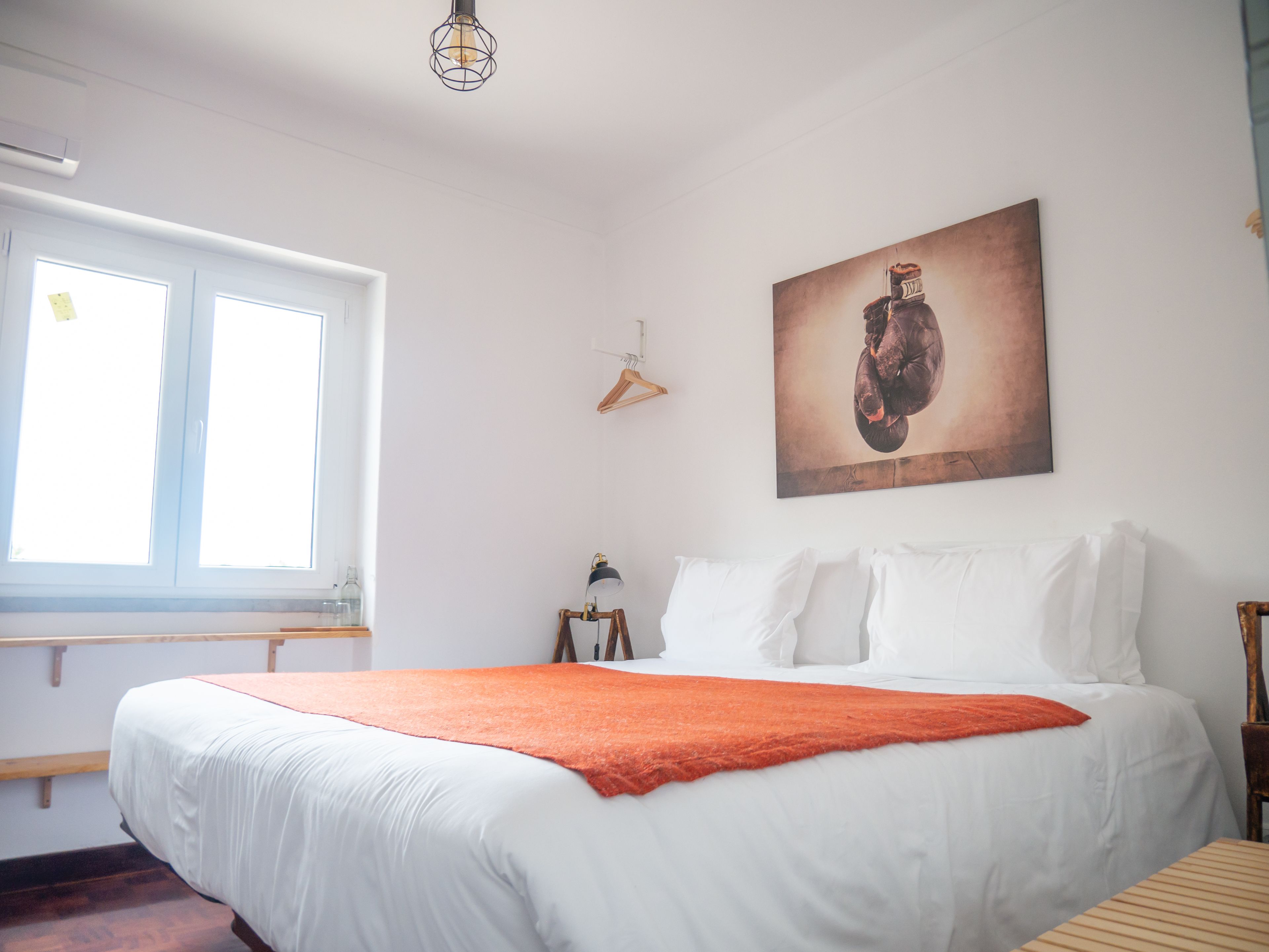 A bedroom with a large bed, a window, a wall-mounted light fixture, and a framed picture.