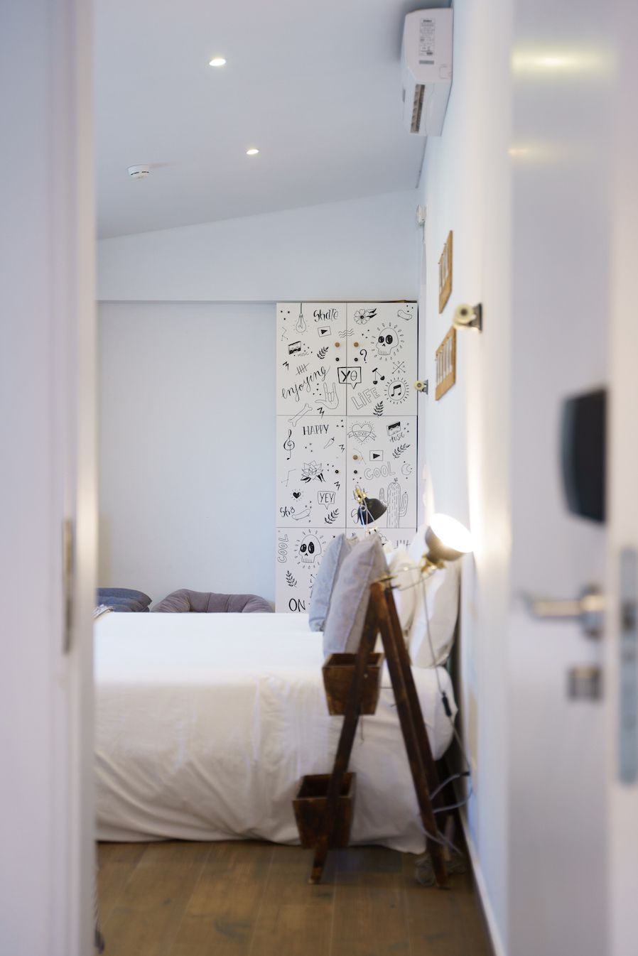 A bedroom with a bed, a wooden ladder, and a wall with various doodles.