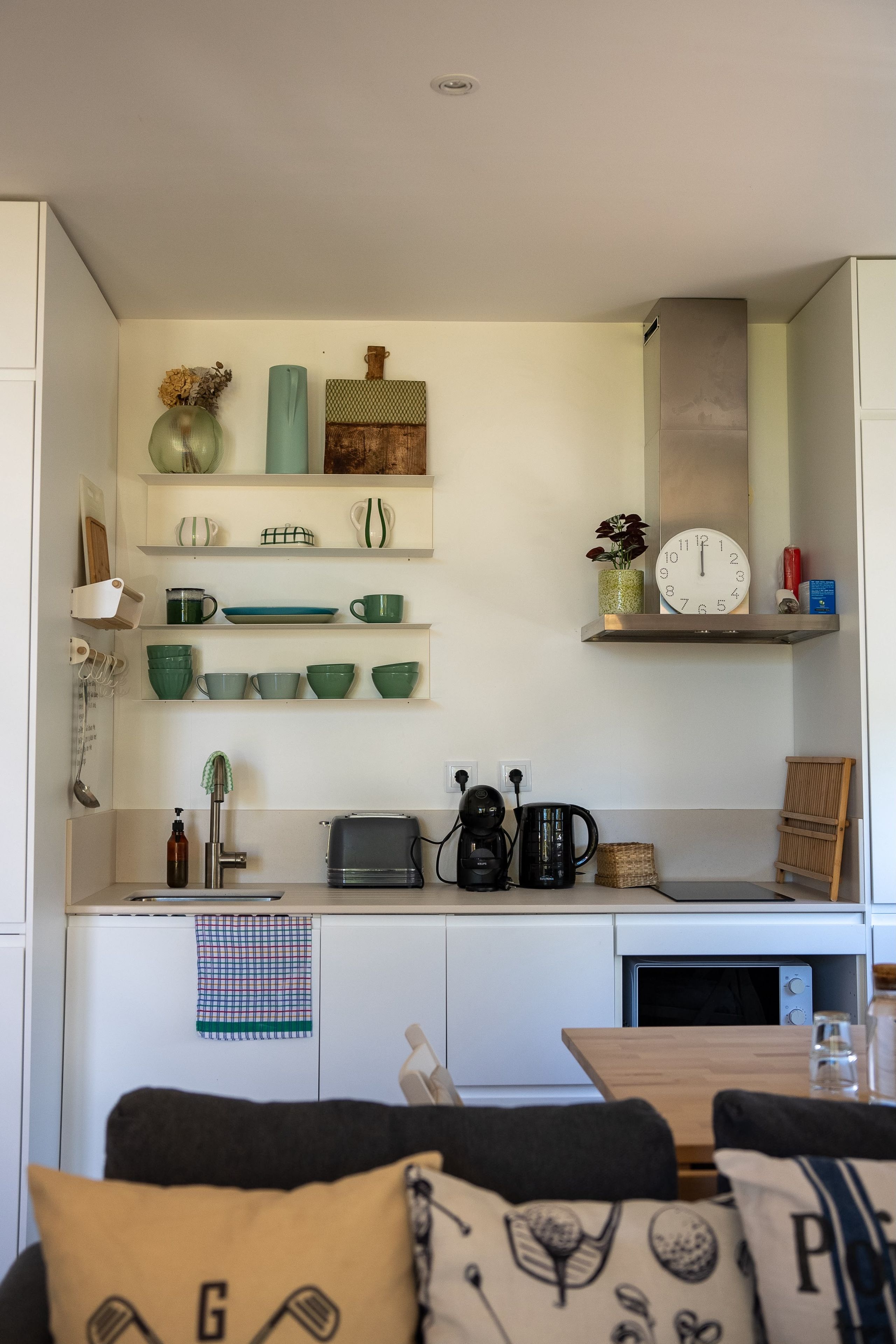A modern kitchen with white cabinets, a coffee maker, a toaster, and a clock on the wall.