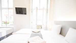 A hotel room with two beds, a flat-screen TV mounted on the wall, and a window with a view of the city. - Narodni Stay (Prague)