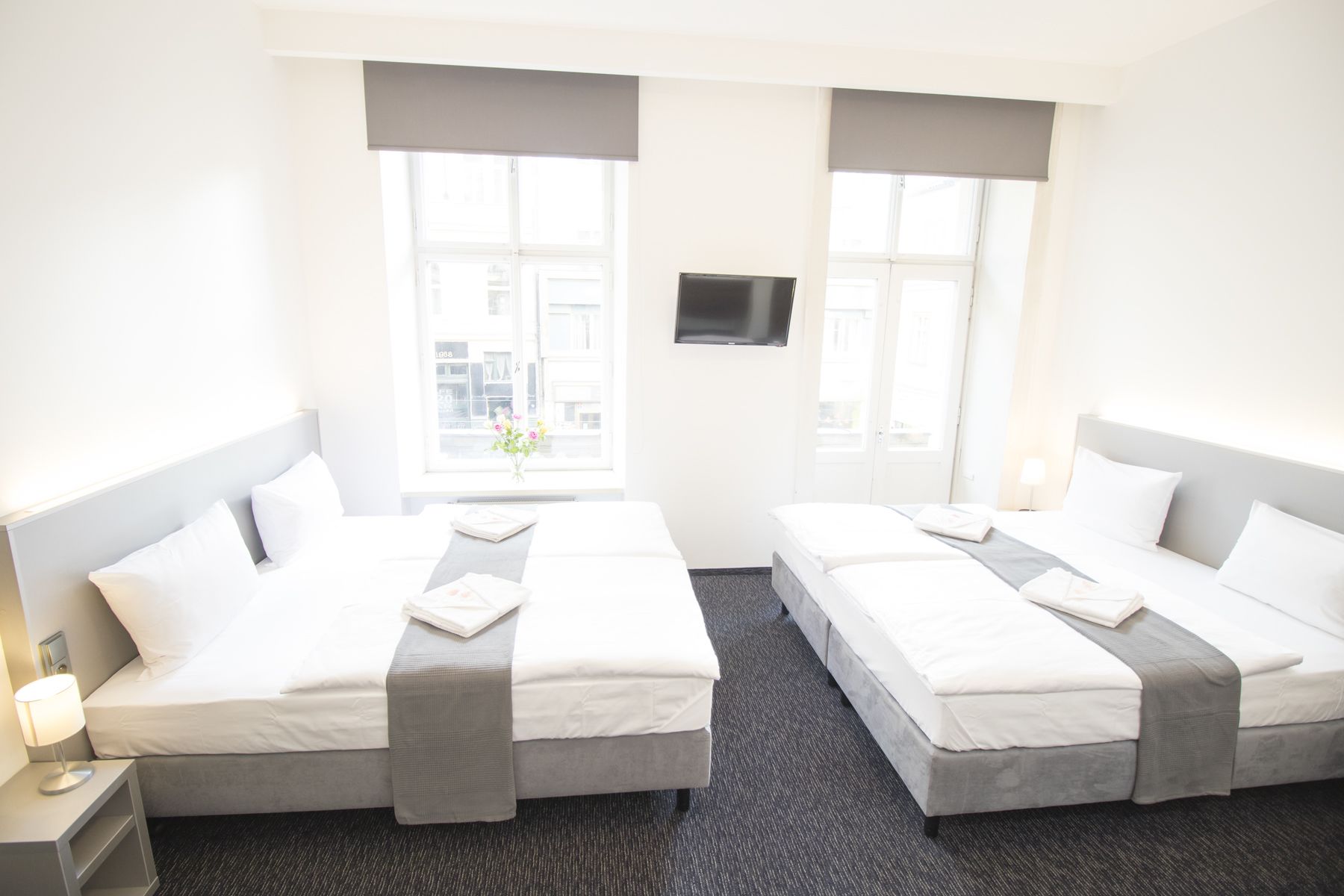 A hotel room with two beds, a TV mounted on the wall, and a window with a view of buildings.