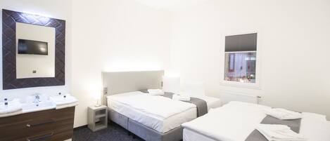 A hotel room with two beds, a large mirror, a TV, a bathroom with a sink and toiletries, and a window with blinds.