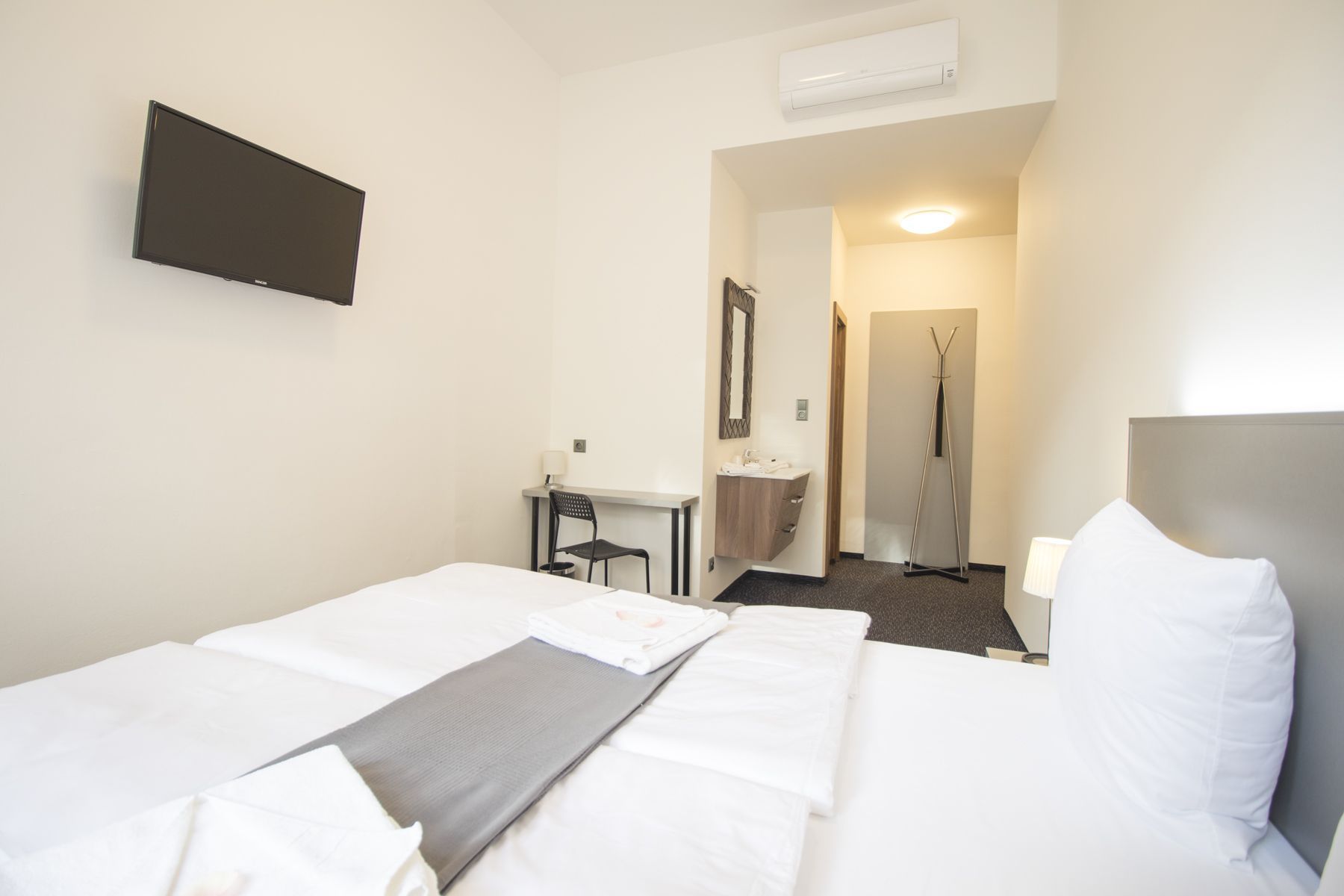 Une chambre d’hôtel équipée d’un lit, d’un bureau, d’une chaise, d’un miroir, d’un lavabo et d’une douche.
