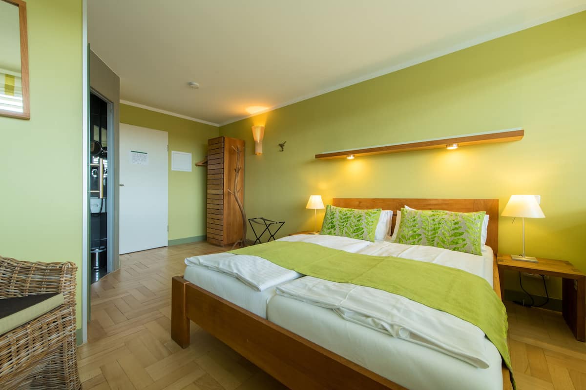 A neatly made bed with a wooden headboard, two bedside lamps, and a green throw blanket.